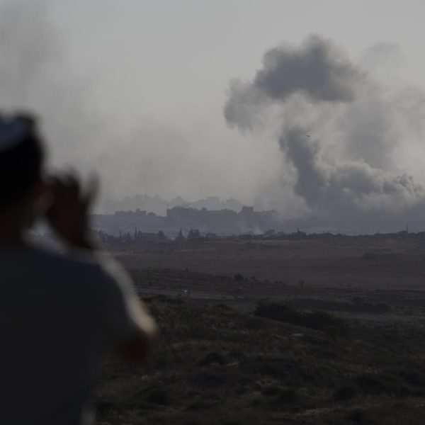 A man watches smoke rising to the sky in the distance.